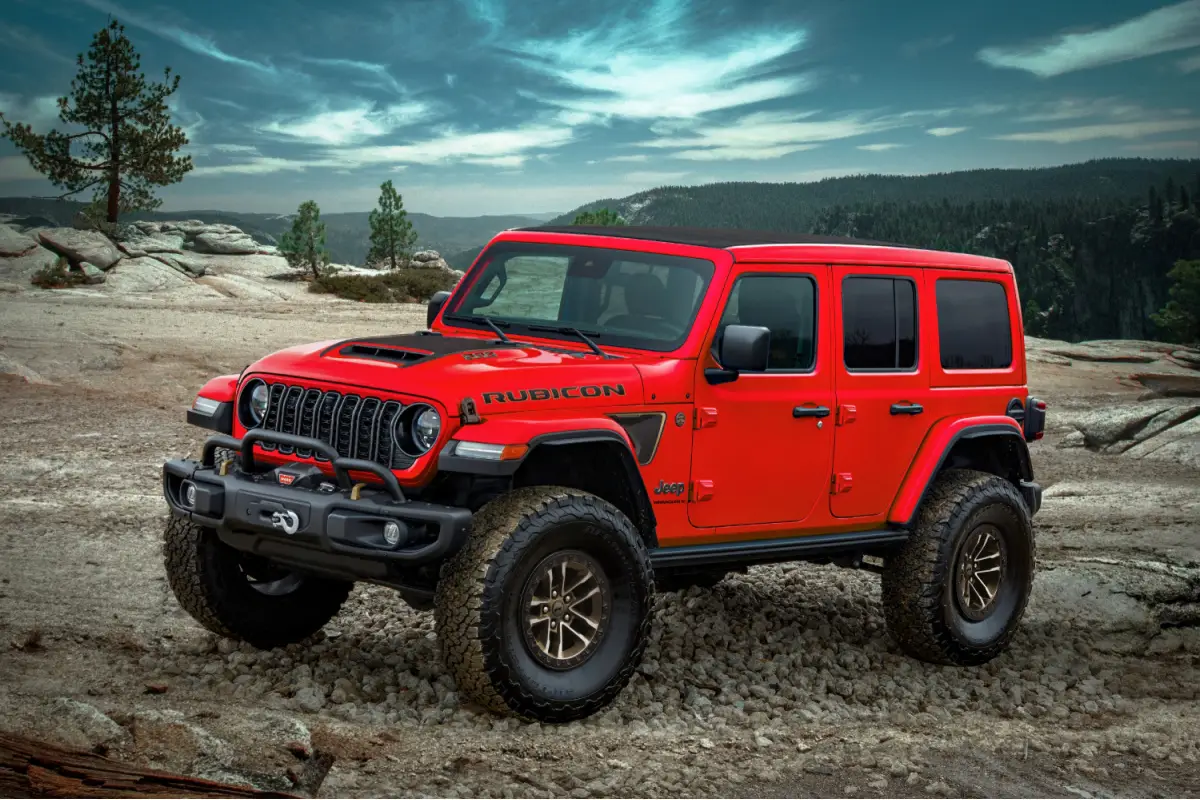 Red Jeep Wrangler Rubicon 4-door SUV parked on a rocky mountain overlook with pine trees and dramatic sky
