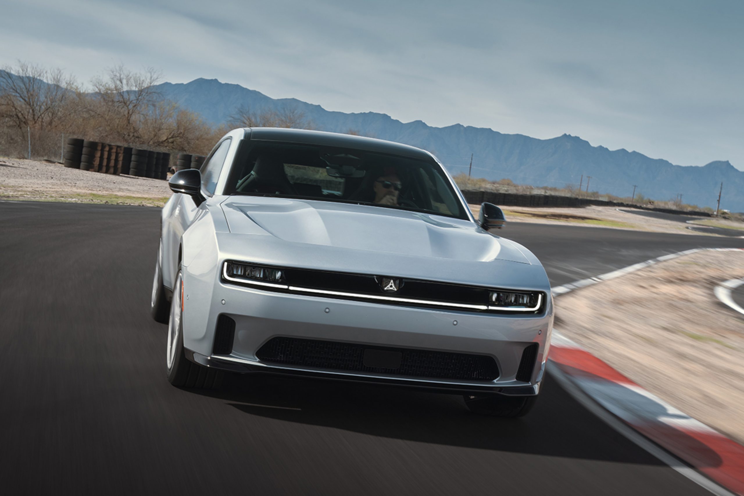 2024 Silver Dodge Charger Daytona electric muscle car driving on a racetrack with mountain backdrop, front view