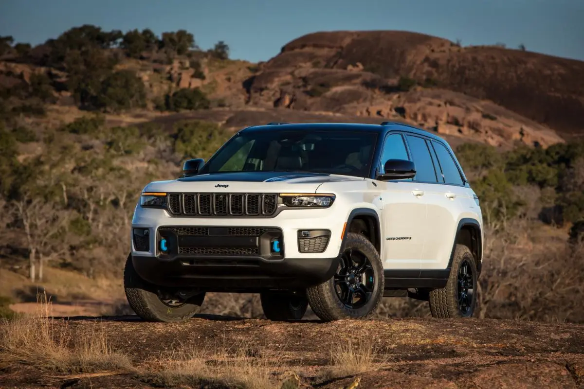 2024 White Jeep Grand Cherokee 4xe SUV parked on a rocky overlook with desert hills in the background