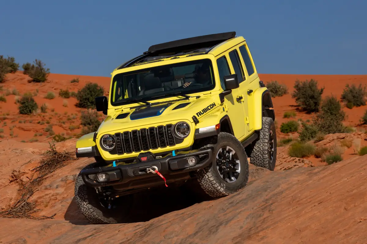 2024 Yellow Jeep Wrangler Rubicon SUV climbing a sandstone rock formation in the desert