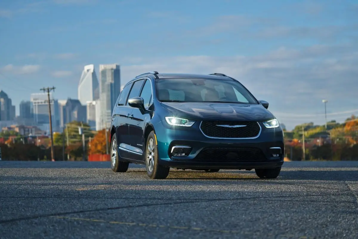 2023 Blue Chrysler Pacifica Hybrid minivan parked with a city skyline in the background at dusk