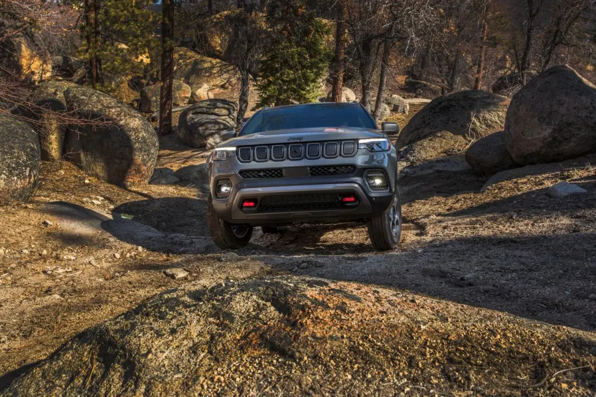 2023 Silver Jeep Compass Trailhawk SUV parked among large boulders on a forest off-road trail, front view