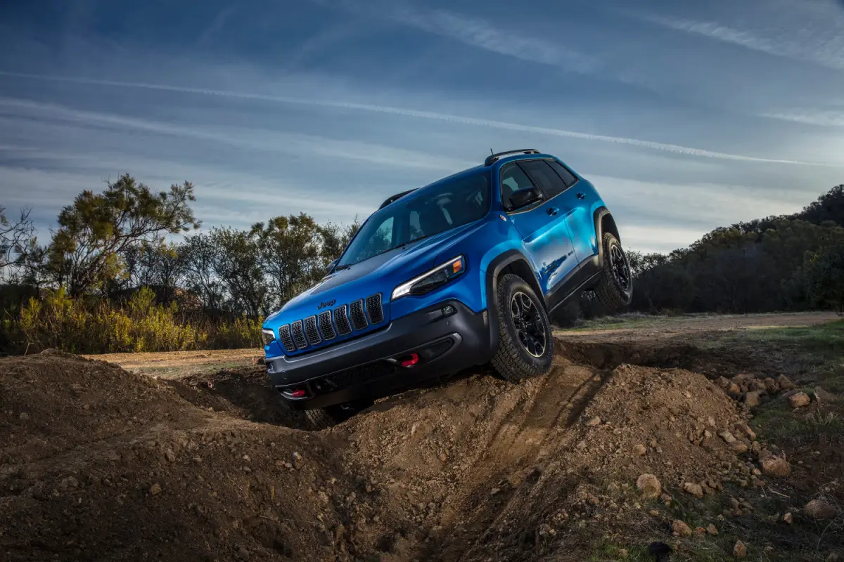 2023 Blue Jeep Cherokee Trailhawk SUV climbing over a dirt mound on an off-road trail at dusk