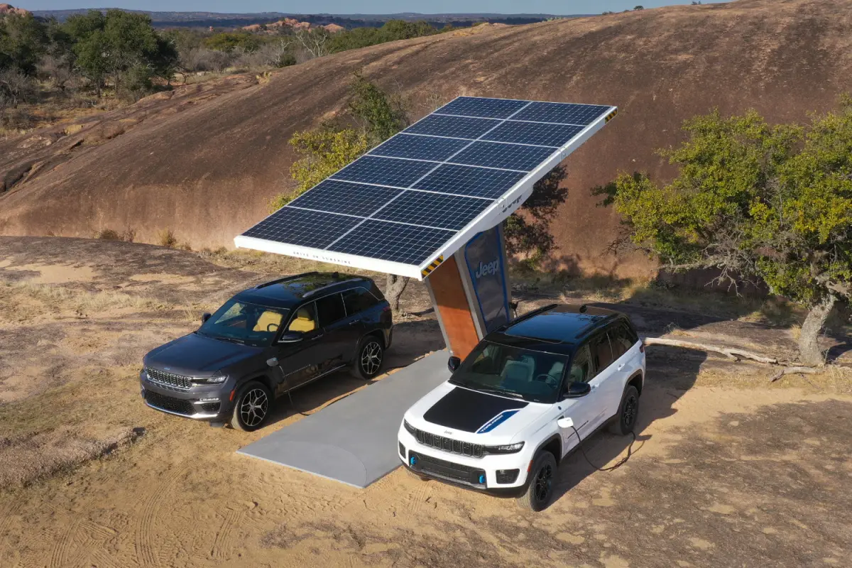 Black and white Jeep Grand Cherokee 4xe plug-in hybrid SUVs charging under a solar panel carport in the desert