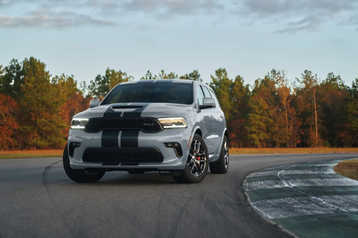 Silver Dodge Durango SRT SUV with black racing stripes parked on a race track surrounded by autumn trees