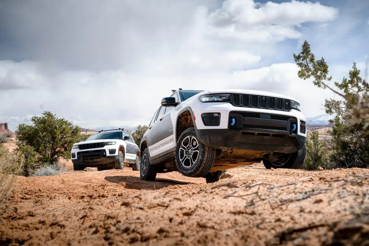White Jeep Grand Cherokee SUVs navigating rocky off-road terrain in a desert canyon