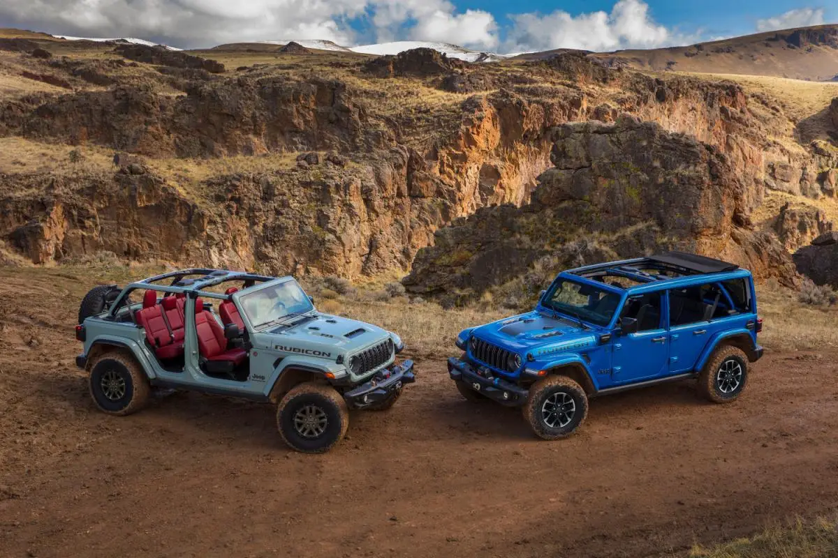 2024 Gray and blue Jeep Wrangler Rubicon SUVs parked side by side on a dirt trail with canyon cliffs in the background