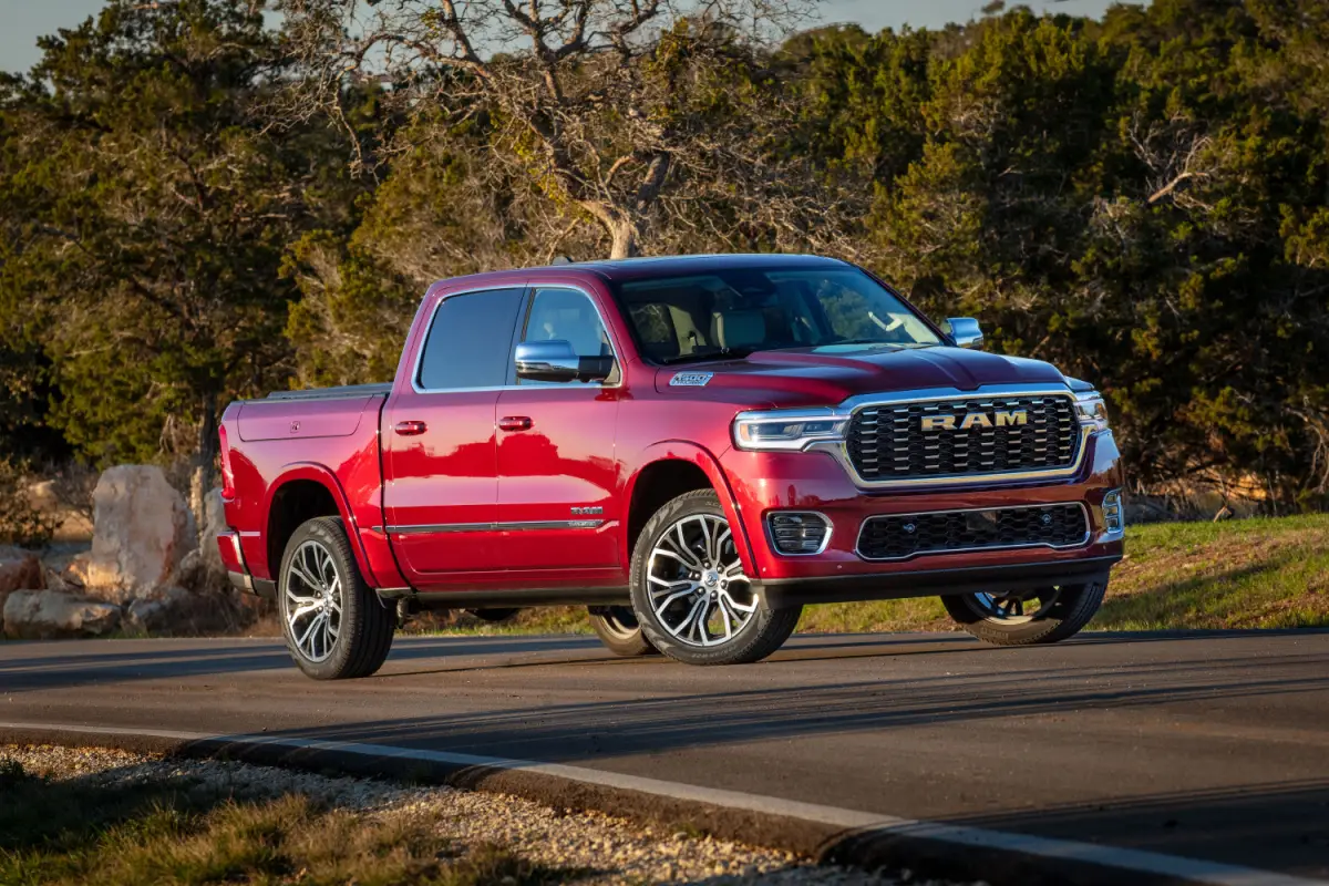 2025 Red Ram 1500 pickup truck driving on a tree-lined country road, front three-quarter view