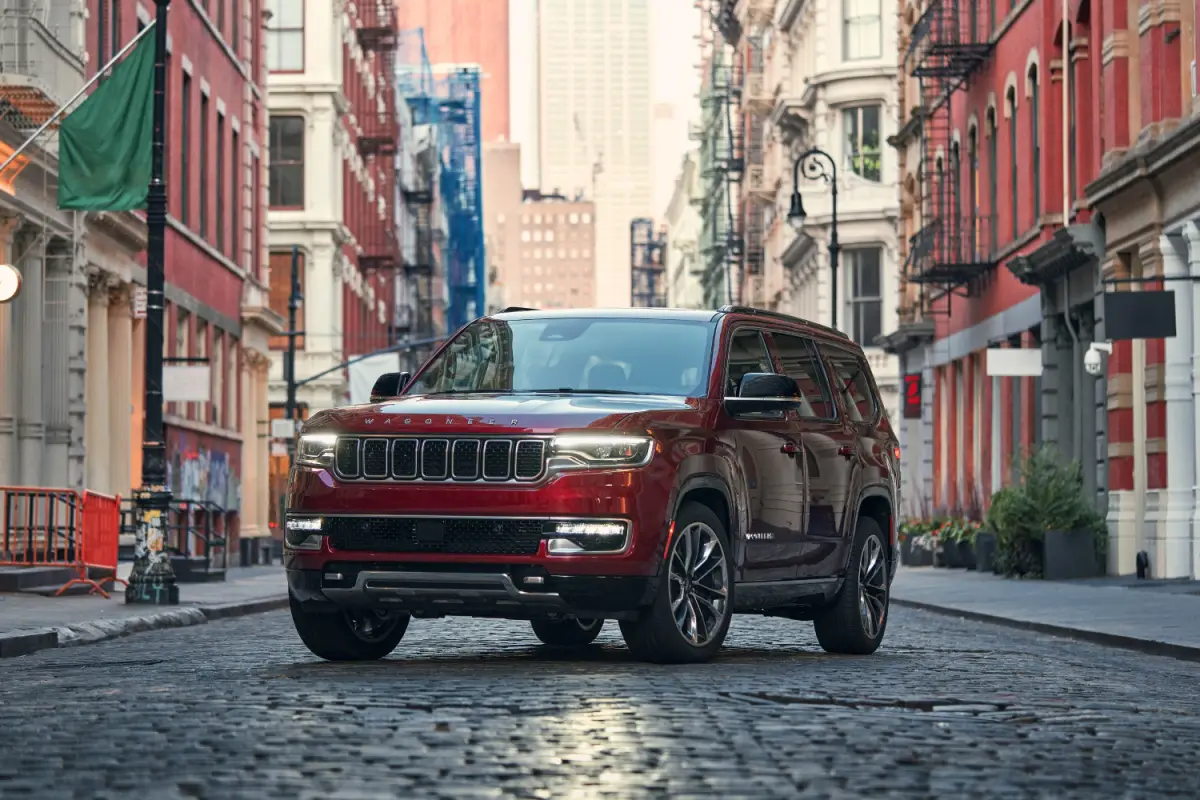 Red Jeep Wagoneer full-size SUV parked on a cobblestone city street lined with historic buildings