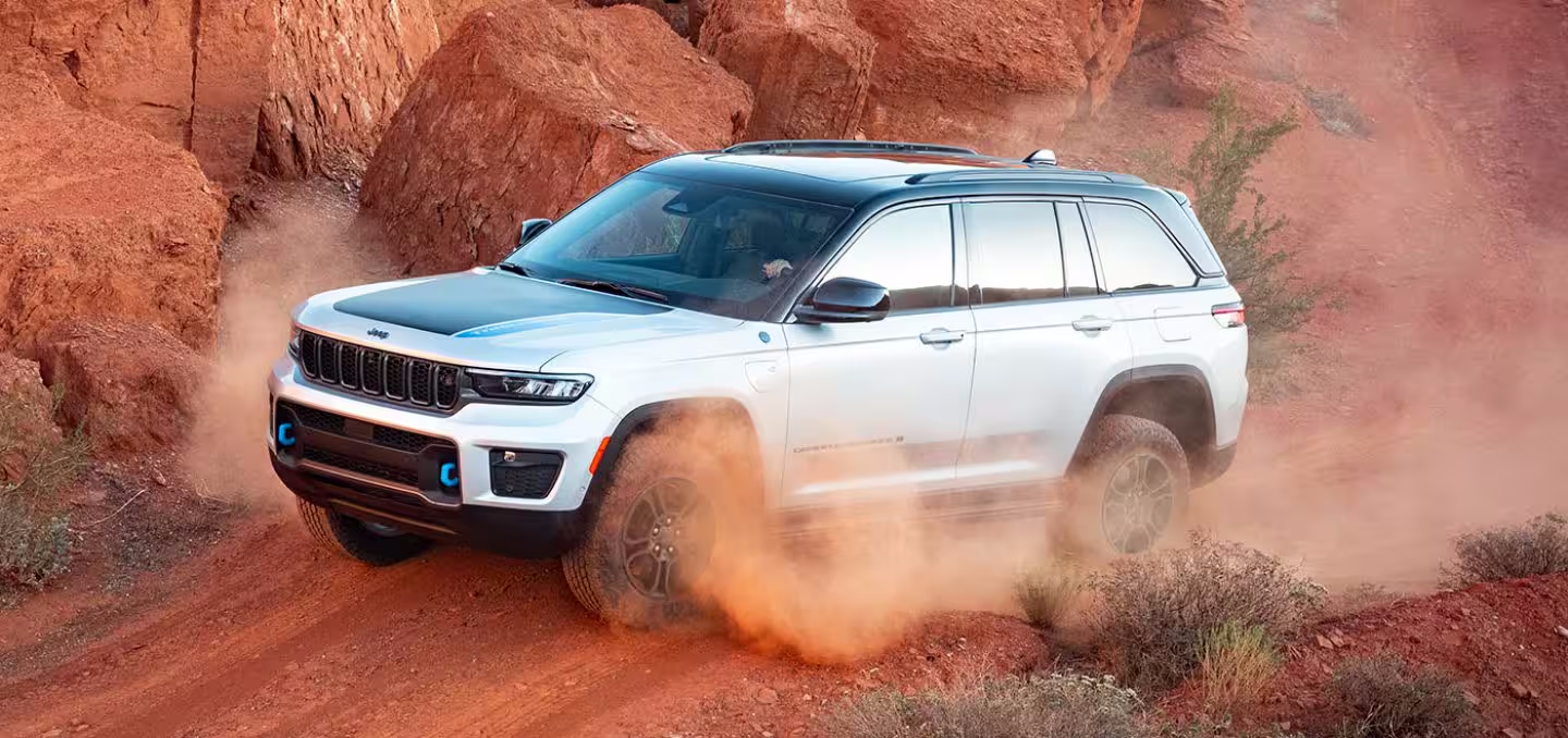 2024 White Jeep Grand Cherokee 4xe plug-in hybrid SUV driving through red rock desert terrain, kicking up dust