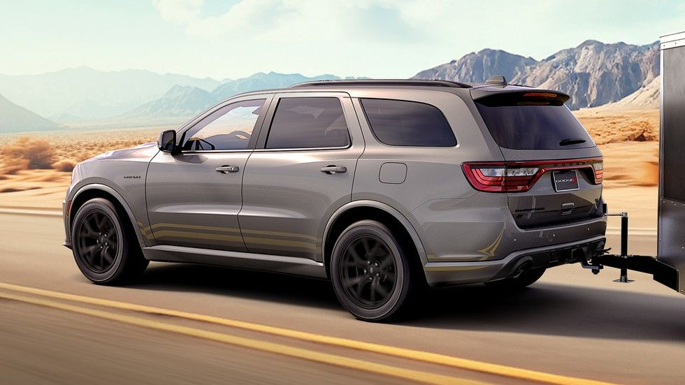 Red Gray Dodge Durango SUV towing a trailer on a desert highway with mountains in the distance