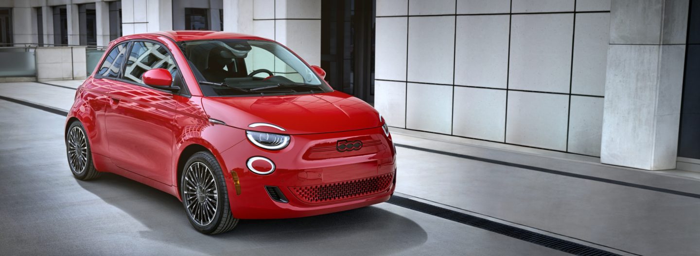 2024 Red Fiat 500e electric car parked outside a modern architectural building