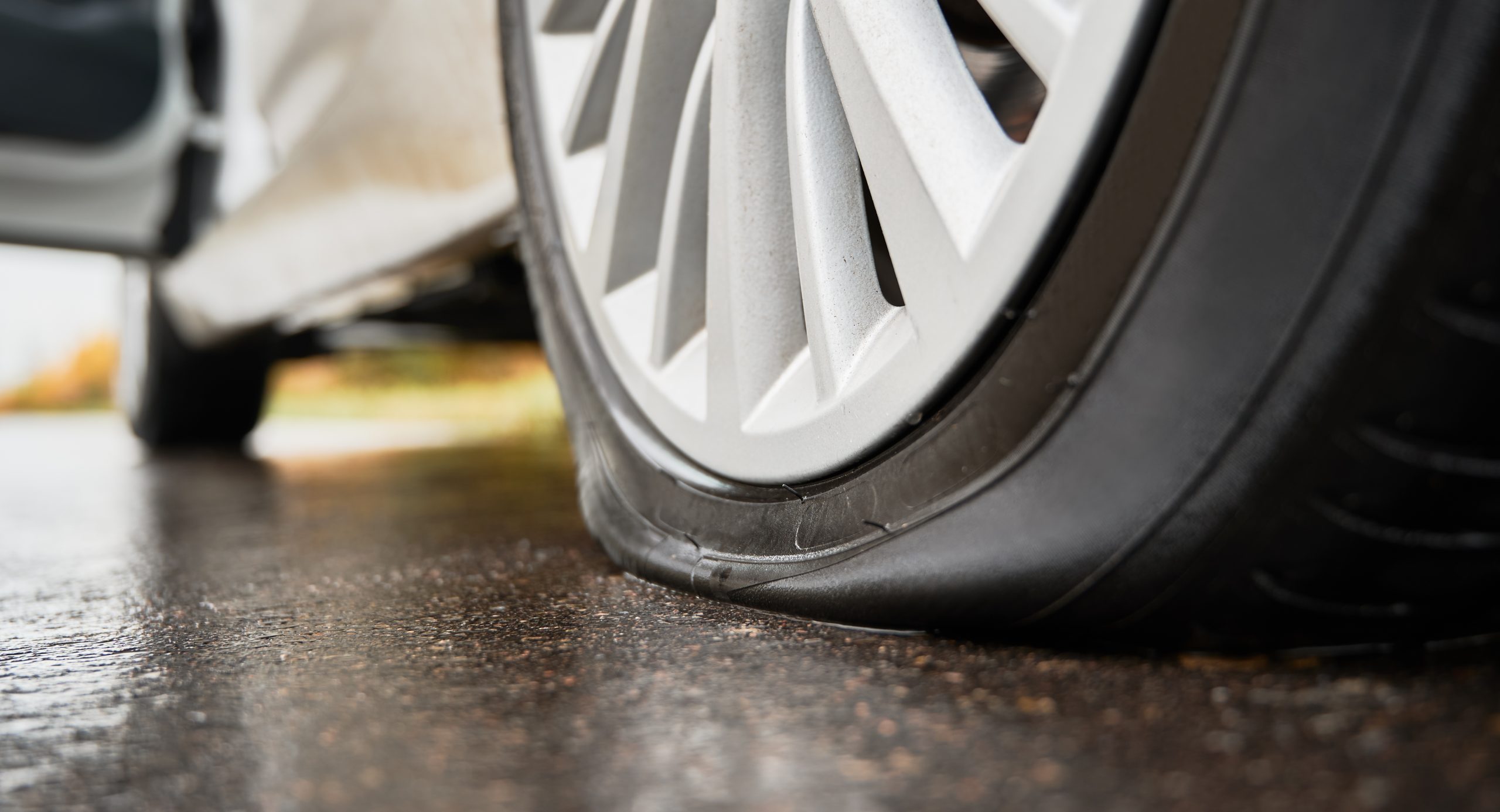 Stopped white car with punctured tire on roadside.